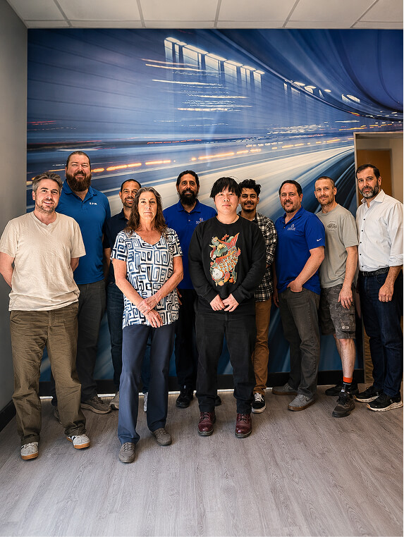 A diverse group of ten people stands smiling in front of a dynamic, blurred cityscape mural, conveying teamwork and positivity in a professional setting.